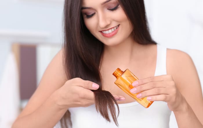 Young woman applying oil onto her hair, indoors